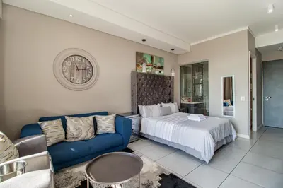 a bedroom with a bed and a couch and a clock at 301 Menlyn Maine Trilogy Apartment in Pretoria