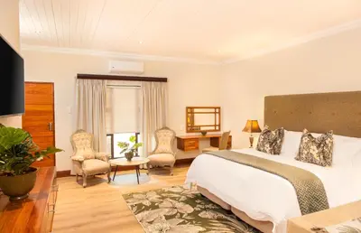 a bedroom with a bed and a desk and chairs at The Coral Tree in Nelspruit
