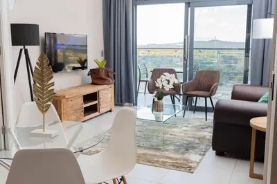 a living room with a glass table and chairs at Menlyn Apartment - 2 Bedroom Apartment in Pretoria