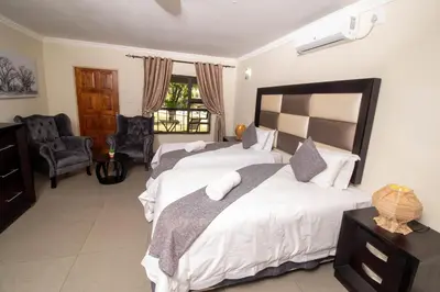 a bedroom with two beds and a chair at ASANTE MOUNTAIN LODGE in Hazyview