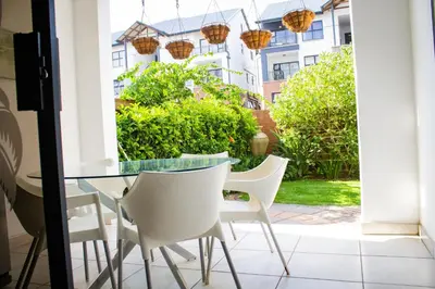 a dining room with a glass table and white chairs at 150 The Blyde Crystal Clear Lagoon 3 Bedroom Garden Apartment in Pretoria