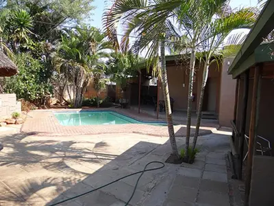 a swimming pool with palm trees next to a house at Lephalale Guest House in Ellisras