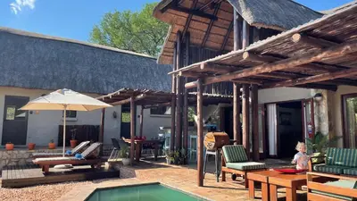 a patio with a pool and a house with an umbrella at Ujabule Lodge in Hoedspruit
