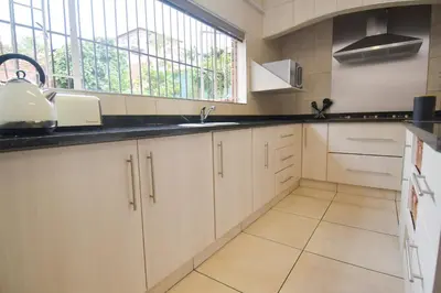a kitchen with white cabinets and a sink and a window at Upmarket Villa with pool & lush garden in Pretoria