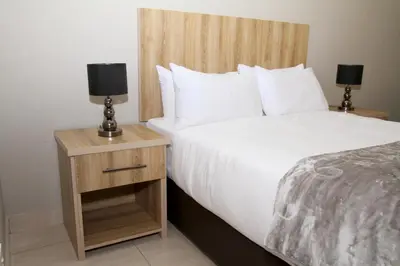 a bedroom with a large bed and a nightstand with a white bedspread at Beautiful Studio Cottage at Menlyn Maine in Pretoria