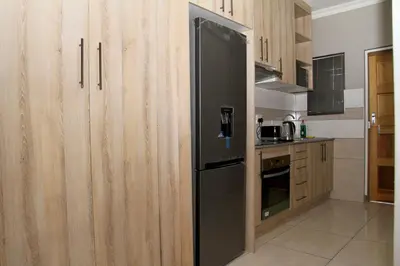 a black refrigerator in a kitchen with wooden cabinets at Beautiful Studio Cottage at Menlyn Maine in Pretoria