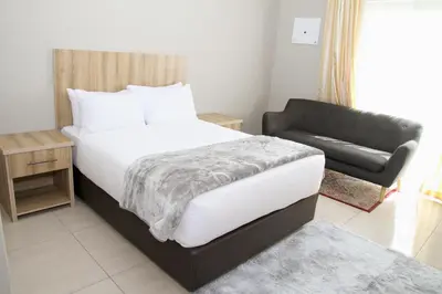 a bedroom with a large bed and a couch at Beautiful Studio Cottage at Menlyn Maine in Pretoria