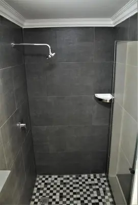 a bathroom with a shower with a tiled floor at Mahem Manor Guesthouse in Brits