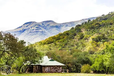 an old house in a field with mountains in the background at Heysbrook Estate - Luxurious lodges in a private valley in Waterval-Onder