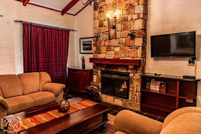 a living room with a stone fireplace and a television at Heysbrook Estate - Luxurious lodges in a private valley in Waterval-Onder