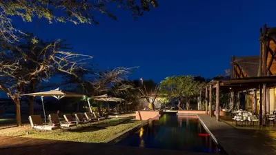 a resort pool with chairs and umbrellas at night at Zebula Boutique Hotel in Mabula