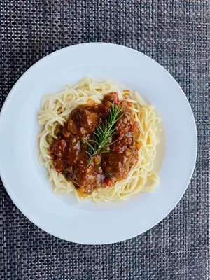 a white plate of spaghetti with meatballs and sauce at Mrhali Boutique Guest House in Kwamhlanga