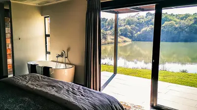 a bedroom with a tub and a view of a lake at Lodge @ Bankenkloof Private Game Reserve in Tierpoort