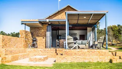 a brick house with a patio with chairs and a table at Lodge @ Bankenkloof Private Game Reserve in Tierpoort