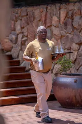 a man holding a tray with glasses and a microphone at Sediba Luxury Safari Lodge in Welgevonden Game Reserve