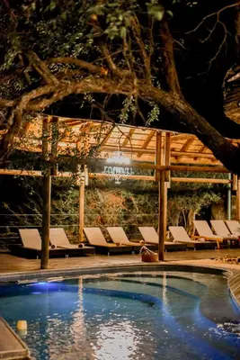 a pool with lounge chairs next to a stone wall at Moditlo River Lodge in Hoedspruit