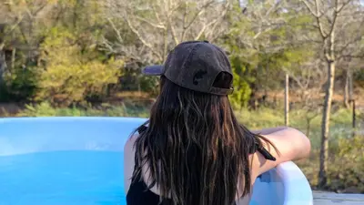 a woman wearing a hat holding a surfboard by a pool at Mologa River Lodge in Rust de Winter