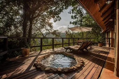 a deck with a hot tub and a bench and an umbrella at Tanamera Lodge in Hazyview