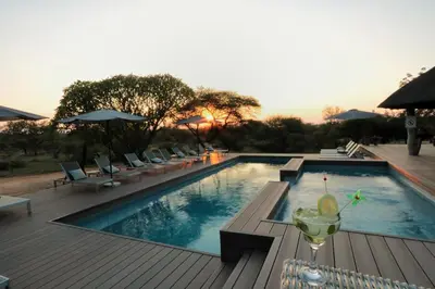 a swimming pool with a drink on a wooden deck at Tshukudu Game Lodge in Hoedspruit