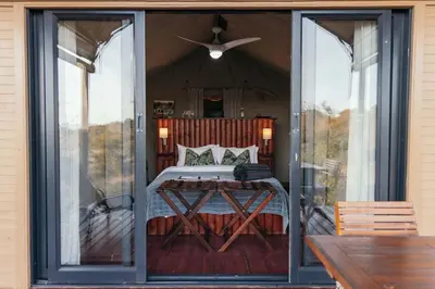 a bedroom with a bed on a porch with sliding glass doors at Isambane Camp in Balule Game Reserve