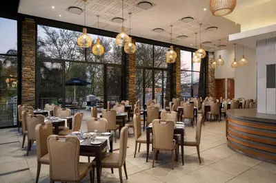 a dining room with tables and chairs and windows at Premier Hotel Midrand in Midrand