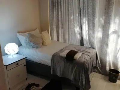 a small bedroom with a bed and a lamp and curtains at Montana Guest House in Pretoria