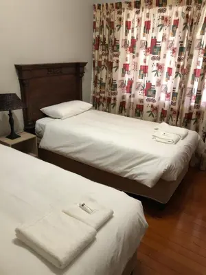 a bedroom with two beds with white sheets and a curtain at Muckleneuk Guest House in Pretoria