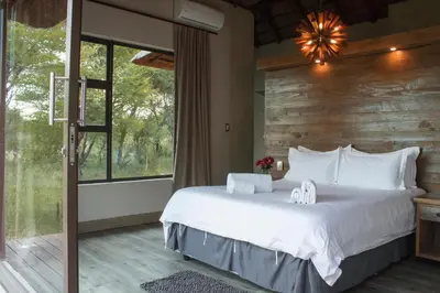 a bedroom with a large bed and a large window at Duiker lodge in Mmukubyane