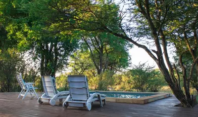 two chairs sitting on a deck next to a swimming pool at Duiker lodge in Mmukubyane