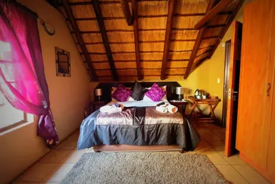 a bedroom with a bed with purple pillows at Khaya Umdani Guest Houses in Marloth Park