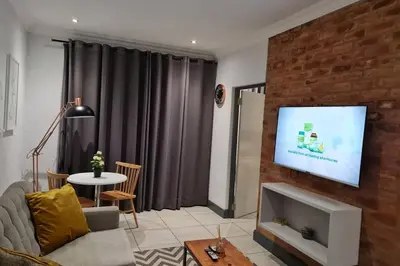 a living room with a couch and a tv on a brick wall at Upmarket one-bedroom apartment at Menlo Park in Pretoria