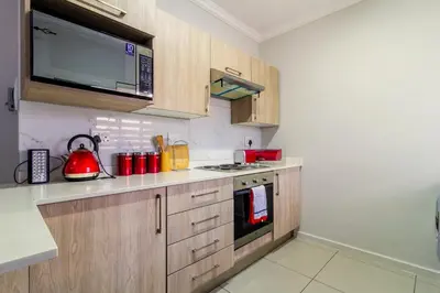 a kitchen with wooden cabinets and a red tea kettle at Buckingham Palace 2 Bed 2 Bath in Midrand