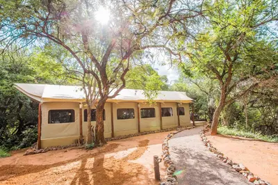 a yellow building with trees and a dirt road at Zwartkloof Adventures Tented Camp in Bela-Bela