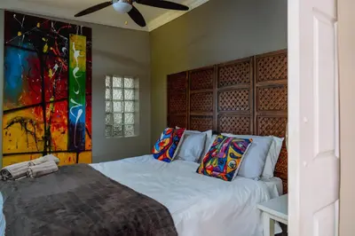 a bedroom with a bed with white sheets and colorful pillows at GILLFORD GALLERY ACCOMMODATION in Benoni