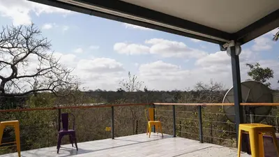 a deck with chairs and a view of the forest at SleepOver Kruger Gate in Skukuza