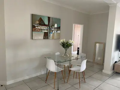 a dining room with a glass table and white chairs at The Blyde Magna Host Luxury Apartments in Pretoria