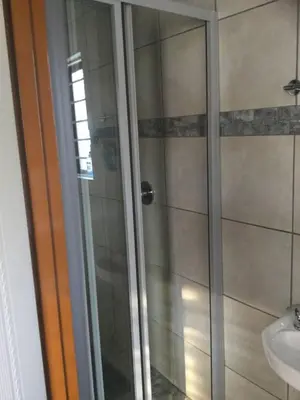 a shower with a glass door next to a sink at Ruros Guest House in Kempton Park
