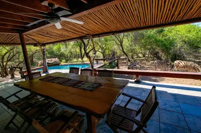 a wooden table and chairs on a patio with zebras at Adventure Bush Villa in Marloth Park