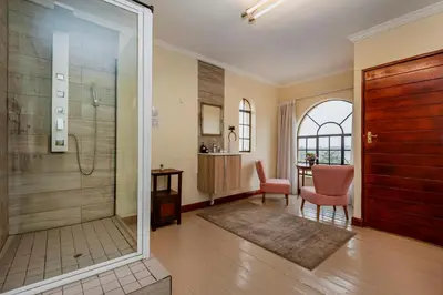 a bathroom with a shower and a chair and a table at Airport Tower Lodge in Kempton Park