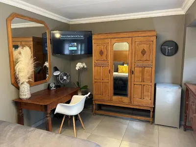 a bedroom with a desk and a dresser and a mirror at Battiss Guest House in Pretoria