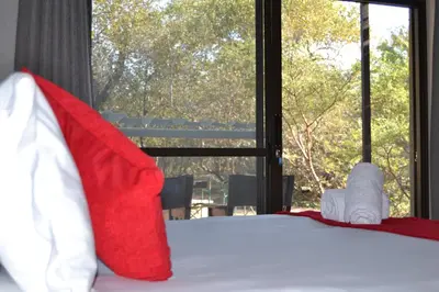 a bed with red and white pillows and a window at Fairfarren in Hoedspruit