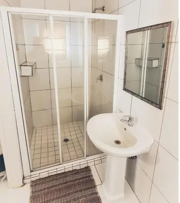 a white bathroom with a shower and a sink at Sheilas Self-Catering Overnight Accommodation in Polokwane