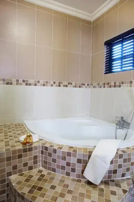 a bath tub in a tiled bathroom with a window at Eco Park Lodge in Centurion