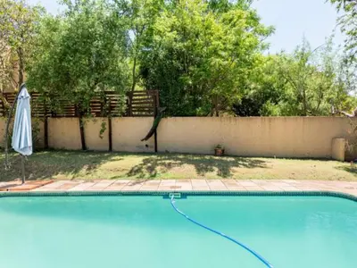 a swimming pool in a yard with a fence and an umbrella at 1 Bedroom Cottage in Midrand