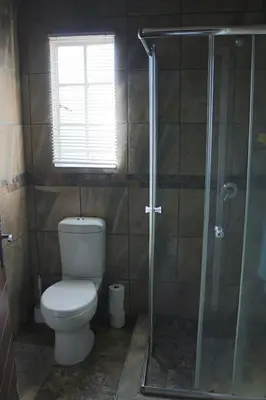 a bathroom with a toilet and a glass shower at Mellivora Lodge in Marloth Park
