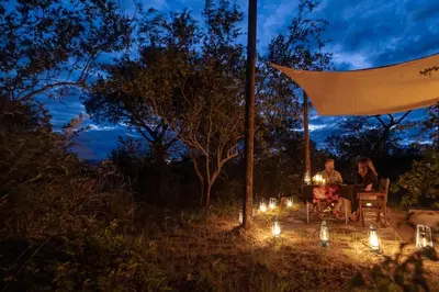 two people sitting at a table with lights at night at Oase by 7 Star Lodges - Greater Kruger Private 530ha Reserve in Hoedspruit
