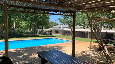 a wooden bench sitting under a pergola next to a swimming pool at Stay Harties Accommodation in Hartbeespoort
