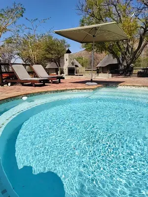 a large blue swimming pool with an umbrella at Milkwood Valley Lodge, Mabalingwe in Bela-Bela