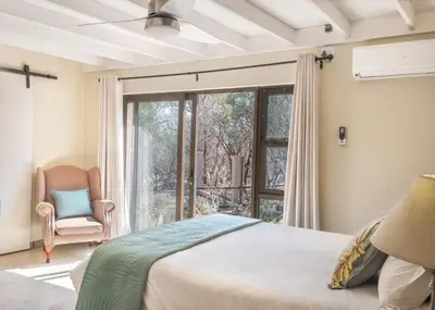 a bedroom with a bed and a window and a chair at The Aloes Bush Lodge in Marloth Park