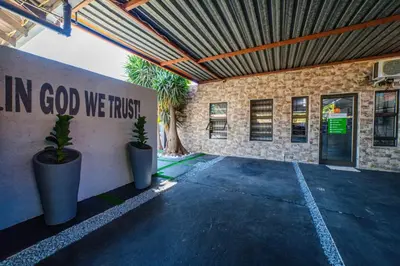 a building with two potted plants and a sign that reads in god we trust at Homes of Ace Executive in Pretoria